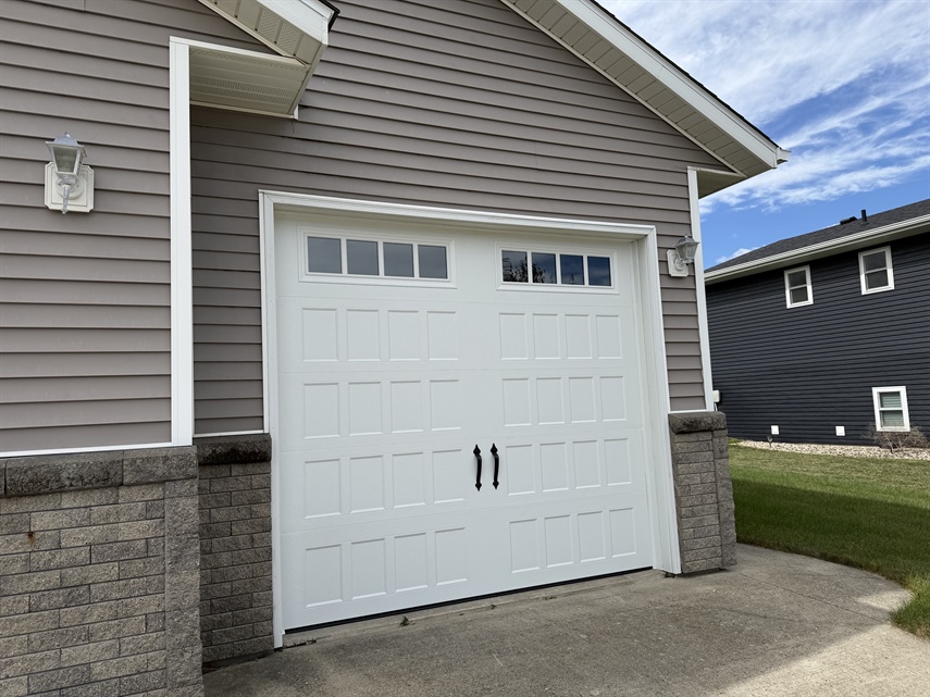 Close-up of a white insulated carriage-style garage door featuring decorative windows and handles in New Ulm, MN.