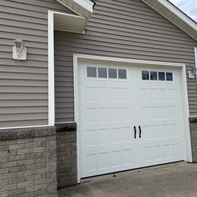 Close-up of a white insulated carriage-style garage door featuring decorative windows and handles in New Ulm, MN.